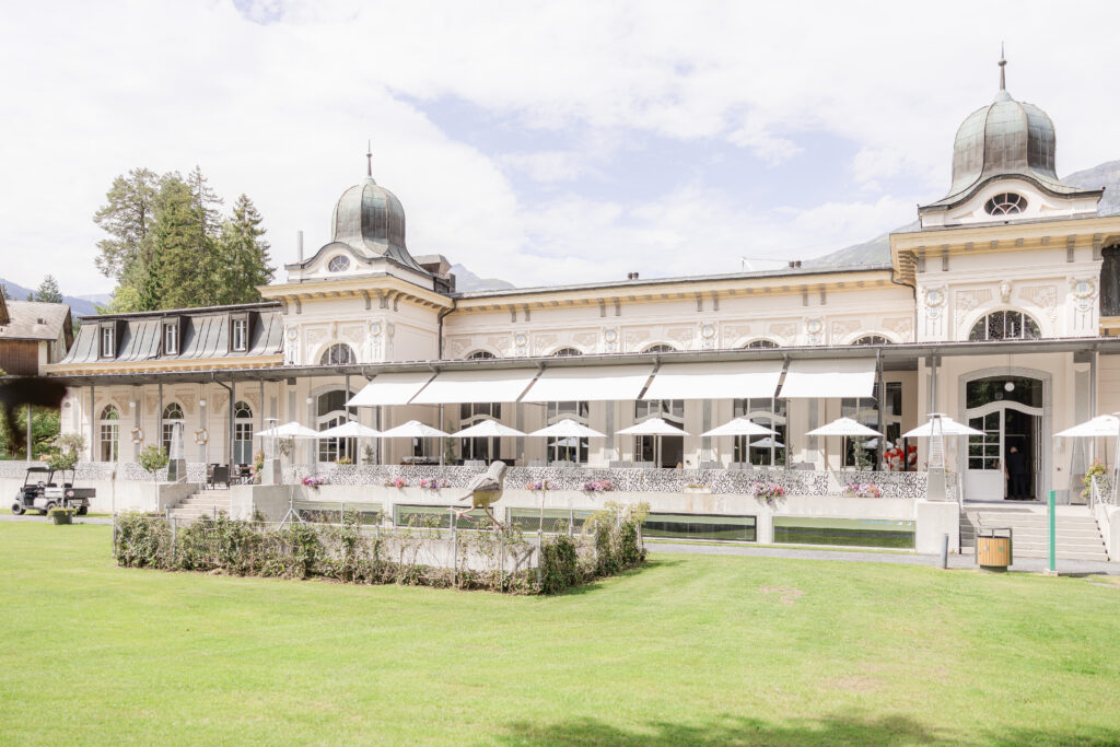 Elegantes historisches Gebäude mit Kuppeltürmen, großen Fenstern und Terrassenschirmen auf einem üppigen grünen Rasen - ein idealer Ort für eine Traurednerin in Zürich oder überall in der Schweiz.